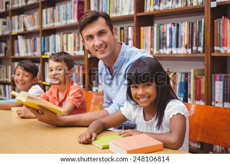 Cute pupils and teacher reading in library at the elementary school