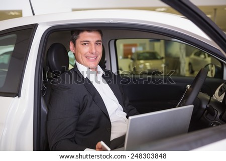 Smiling businessman using laptop in his car at new car showroom