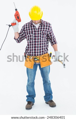 Full length of male repairman holding drill machine and hammer on white background