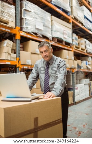 Focused warehouse manager working on laptop in a large warehouse