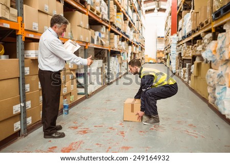Manager watching worker carrying boxes in a large warehouse