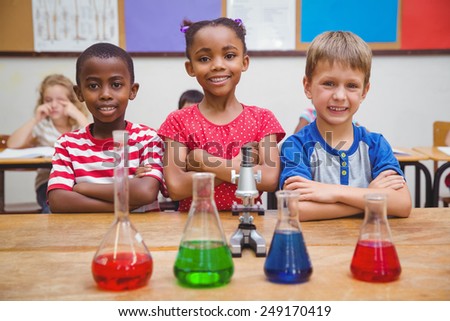 Cute pupils standing with arms crossed behind beaker at the elementary school