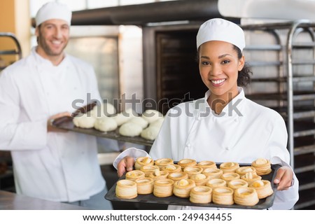 Baker smiling at the camera holding tray in the kitchen of the bakery