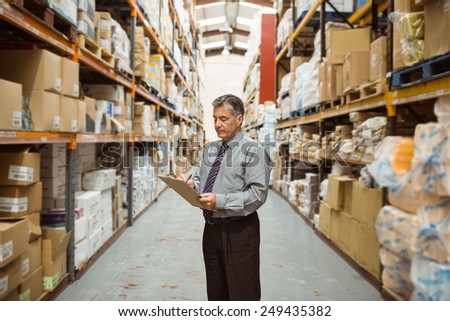 Warehouse manager writing on clipboard in a large warehouse