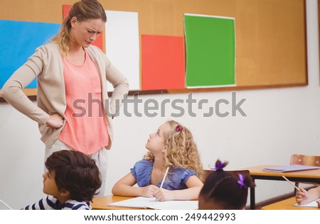Angry teacher looking pupil with hands on hips at the elementary school