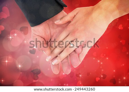 Close-up of bride and groom with hands together against valentines heart design