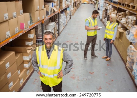 Smiling manager placing his hands on his hips in a large warehouse