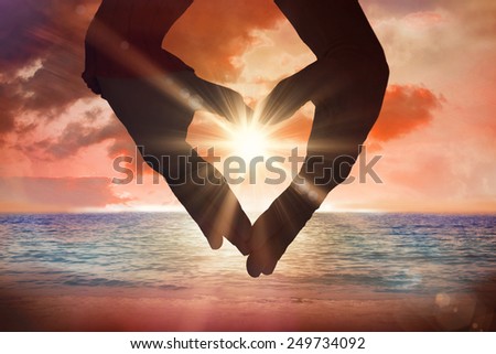 Close up of hands forming heart against sunrise over magical sea