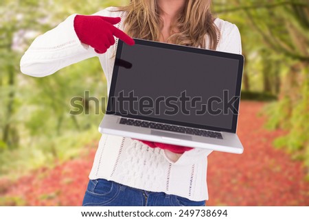 Festive blonde pointing to laptop against peaceful autumn scene in forest