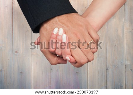 Newlyweds holding hands close up against pale grey wooden planks