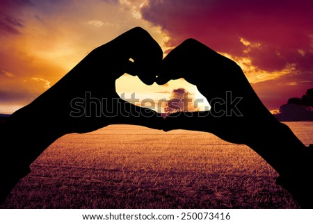 Woman making heart shape with hands against countryside scene