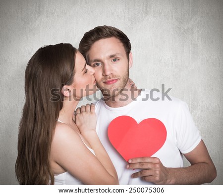 Woman kissing man as he holds heart against weathered surface
