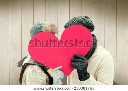 Attractive young couple in warm clothes holding red heart against wooden planks