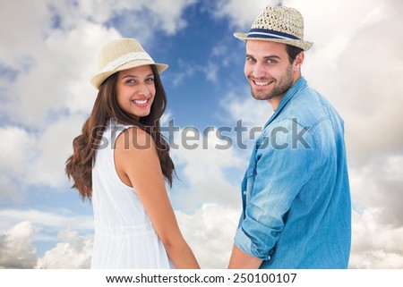 Happy hipster couple holding hands and smiling at camera against blue sky with white clouds