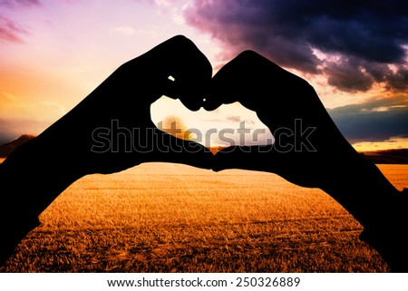 Woman making heart shape with hands against countryside scene