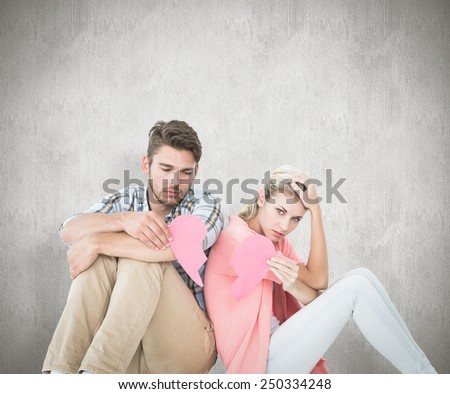 Attractive young couple sitting holding two halves of broken heart against white background
