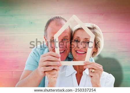 Happy older couple holding house shape against pink and green planks