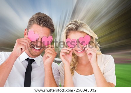 Attractive young couple holding pink hearts over eyes against sunny day by the river