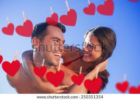 Handsome man carrying his girlfriend on his back against hearts hanging on a line