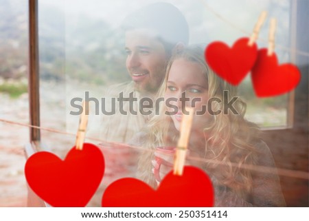 Thoughtful content couple with cups looking through window against hearts hanging on a line