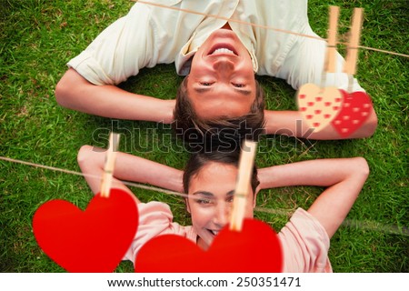 Two friends smiling while lying head to head with both hands behind their neck against hearts hanging on the line