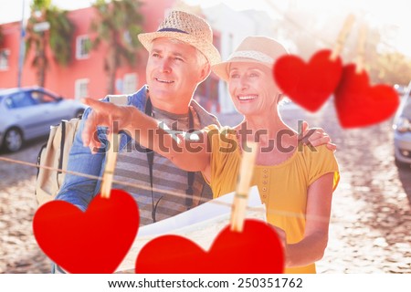 Happy tourist couple using map in the city against hearts hanging on a line