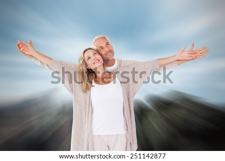 Happy couple standing with arms outstretched against large rock overlooking big city