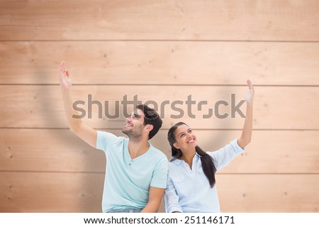 Cute couple sitting with arms raised against overhead of wooden planks
