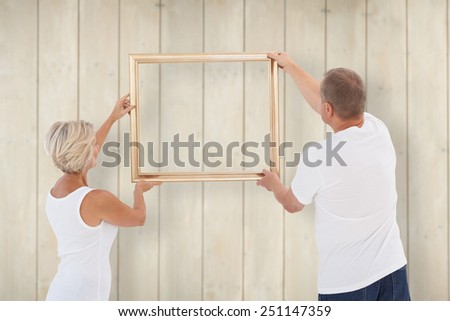 Mature couple hanging up picture frame against wooden planks