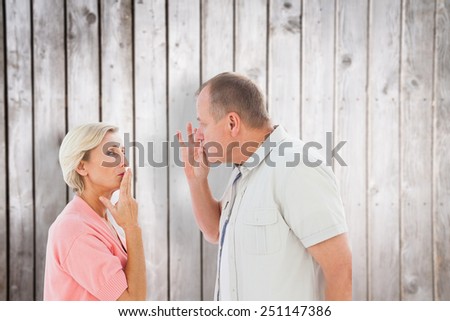 Older couple holding hands to mouth for silence against wooden planks