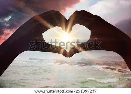 Hands making heart shape on the beach against sunrise over magical sea