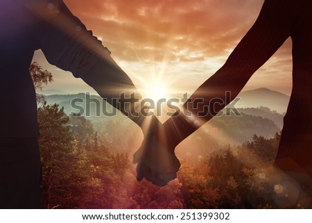 Couple holding hands rear view against sunrise over mountains