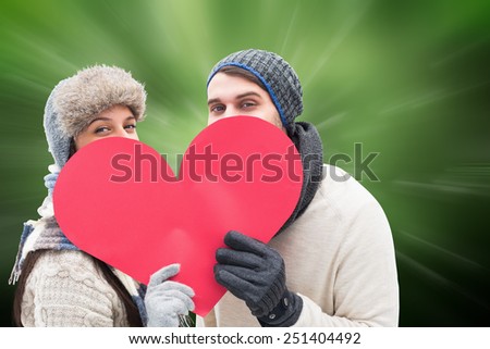Attractive young couple in warm clothes holding red heart against digitally generated dandelion seeds on green background