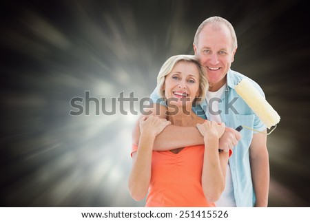 Happy older couple holding paint roller against black abstract light spot design