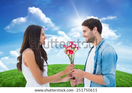 Happy hipster giving his girlfriend roses against green hill under blue sky