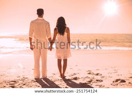Attractive couple holding hands and watching the waves at the beach