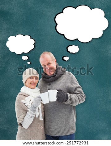 Happy mature couple in winter clothes holding mugs against teal