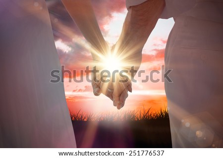 Bride and groom holding hands close up against sunrise over grass