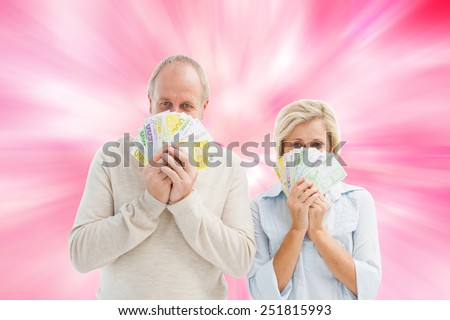Happy mature couple smiling at camera showing money against digitally generated girly heart design