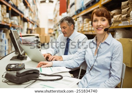Warehouse manager working at her desk wearing headset in a large warehouse