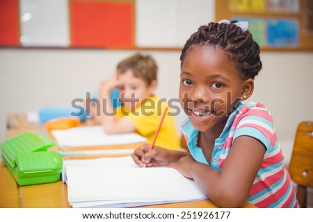 Cute pupils drawing at their desks one smiling at camera at the elementary school