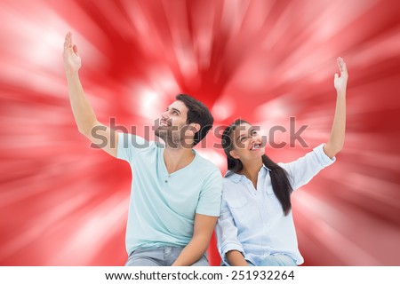 Cute couple sitting with arms raised against digitally generated twinkling light design