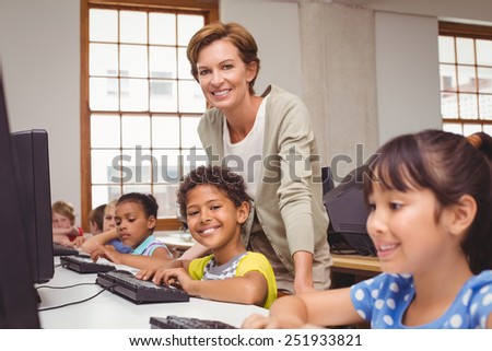 Cute pupil in computer class with teacher smiling at camera at the elementary school