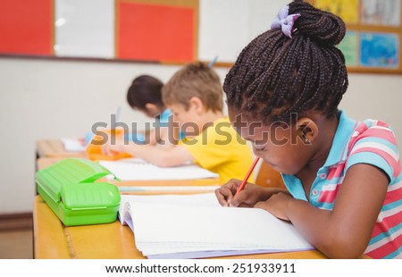 Cute pupils writing at desk in classroom at the elementary school