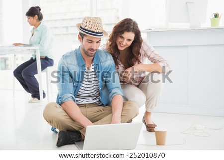 Smiling colleagues sitting on the floor using laptop in the office