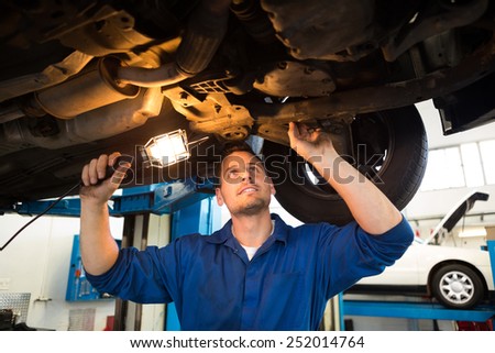 Mechanic shining torch under car at the repair garage