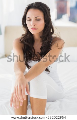 Worried brunette sitting on bed at home in bedroom
