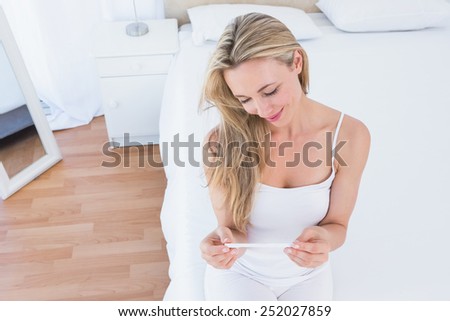 Smiling blonde looking her pregnancy test at home in the bedroom