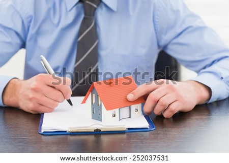 Businessman taking notes and holding miniature house in his office
