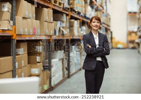 Smiling manager with arms crossed a large warehouse